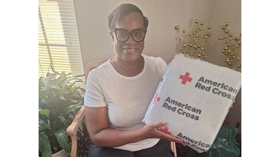 Jane Watson sitting in a chair holding a wrapped Red Cross blanket.