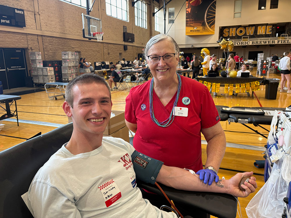 Red Cross phlebotomist Jenise McKee standing next to Jake McCarthy who is sitting in chair about to donate blood.