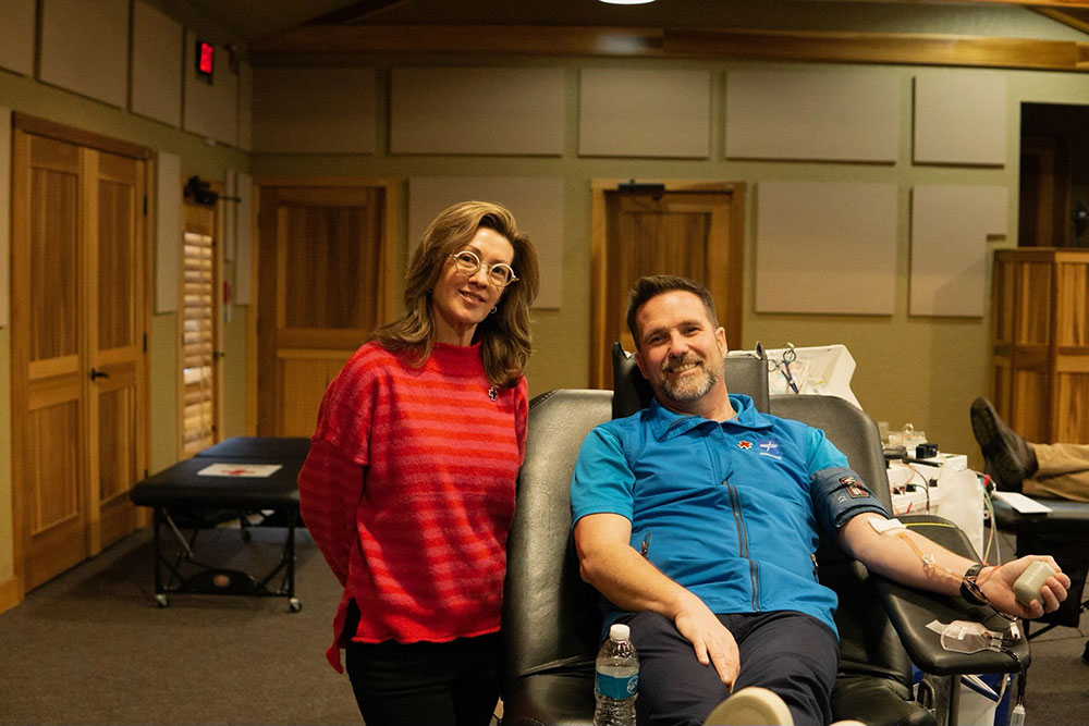 Women standing next to man giving blood in chair