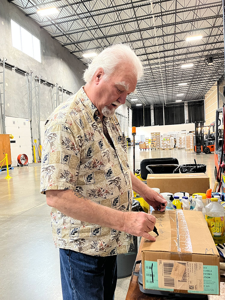 Richard Miller in a warehouse writing on a cardboard box.