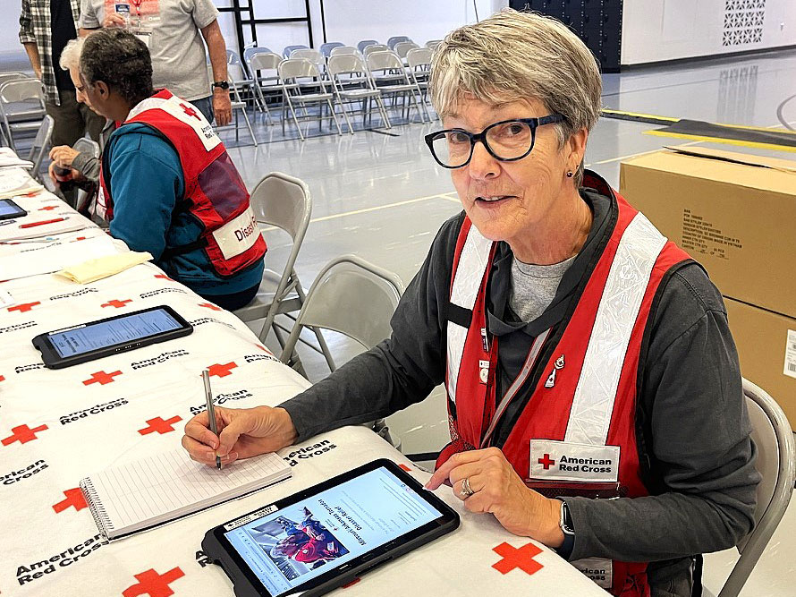 Red Cross volunteer Carol Roam sitting at a table with a tablet and notepad.