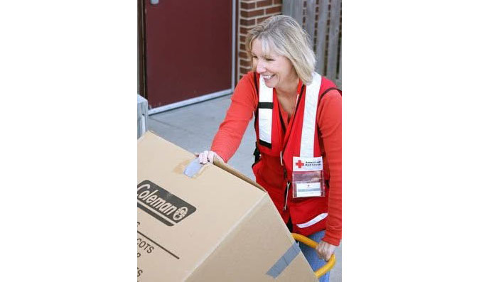 Sherri Odell wearing a Red Cross vest, pushes a hand cart with a large box.