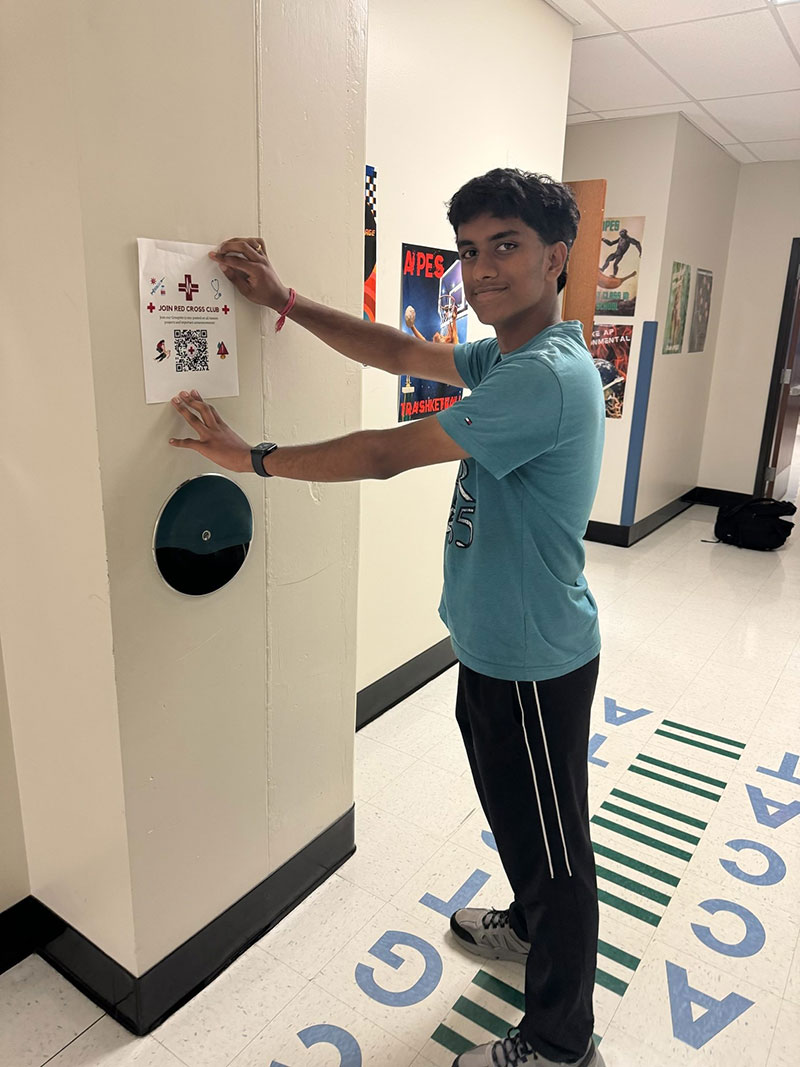 Sid Kaparthi hanging Red Cross flyer in school hallway.