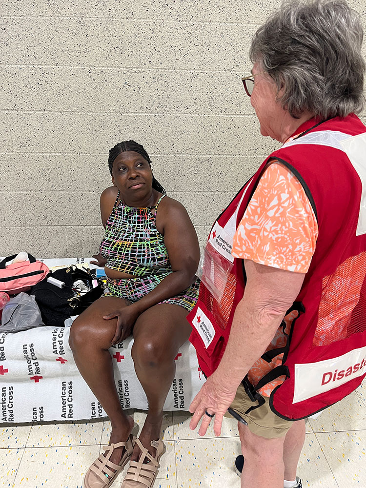 Yolanda Brefford sitting on a shelter bed with a Red Cross volunteer standing next to her.