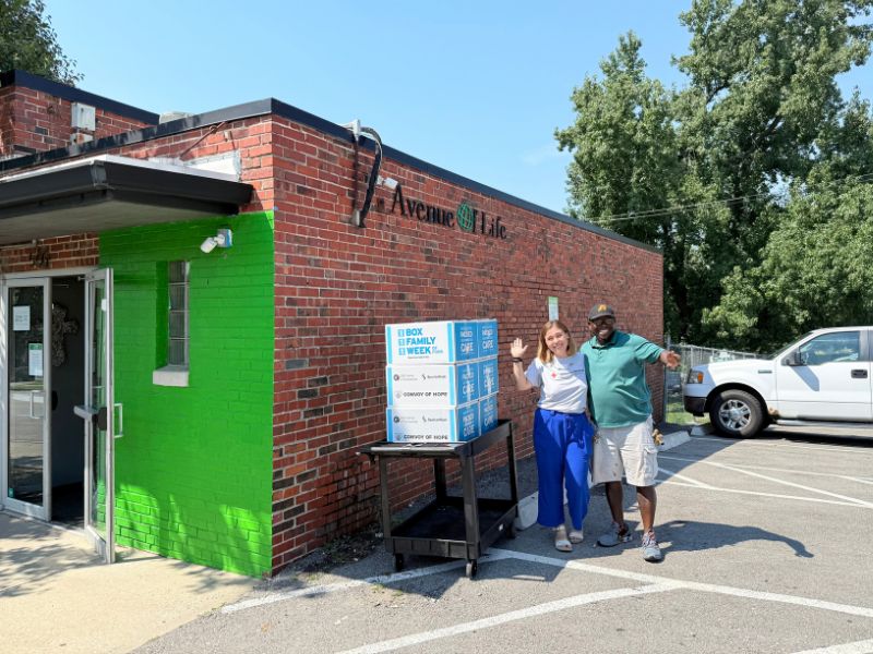 two volunteers standing outside of building with boxes