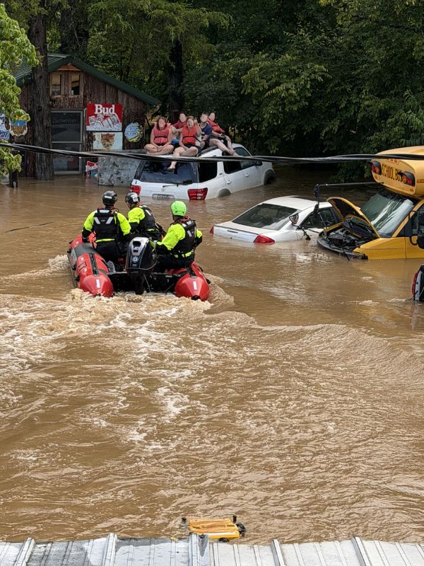 rescuers on boat in flooded area drive toward civilians on top of vehicle