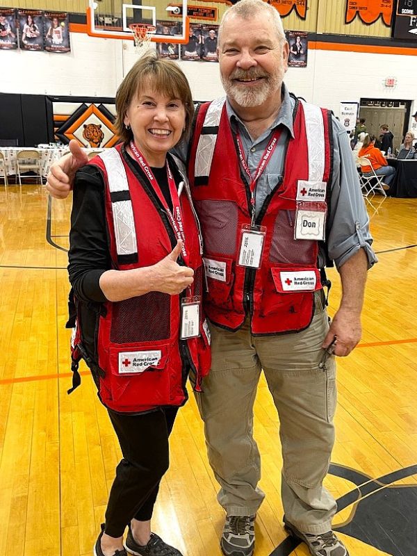 volunteers patsy and don smiling with red cross gear on.