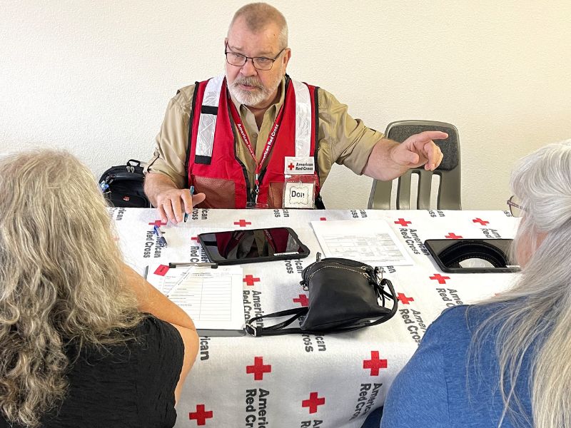 volunteer talking with two people at red cross table.