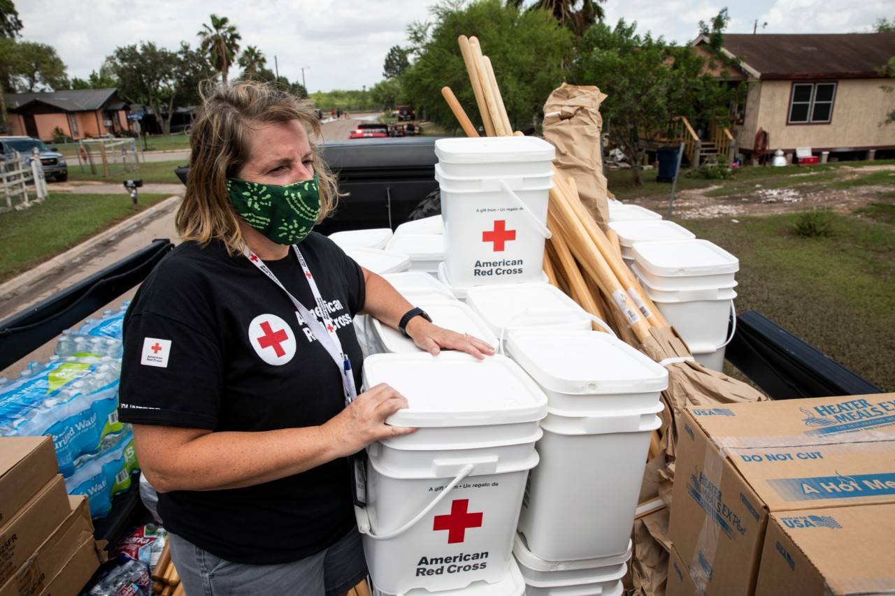 July 30, 2020. Mercedes, Texas.American Red Cross volunteer Pam Simone catches a ride with the fire department delivering items to be given to families in an area affected by Hurricane Hanna in Mercedes, TX on Thursday July 30, 2020. The Red Cross teamed up with the local fire department to drive through neighborhoods and hand out cleaning kits, rakes, shovels, water and tarps to those in need.Photo by Scott Dalton/American Red Cross