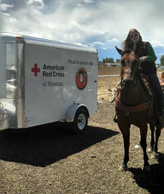 Red Cross female employee on horseback in front of Red Cross trailer.