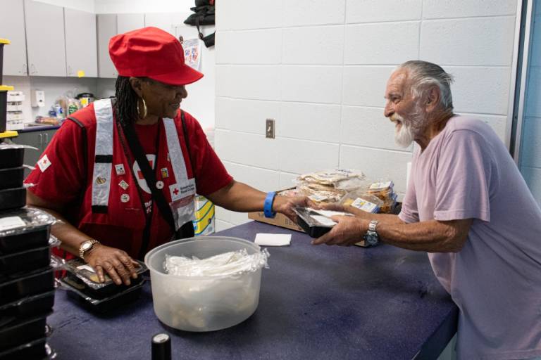 Red Cross volunteer Essie Hopkins hands a meal to a person staying in a Red Cross shelter after Hurricane Milton in 2024.