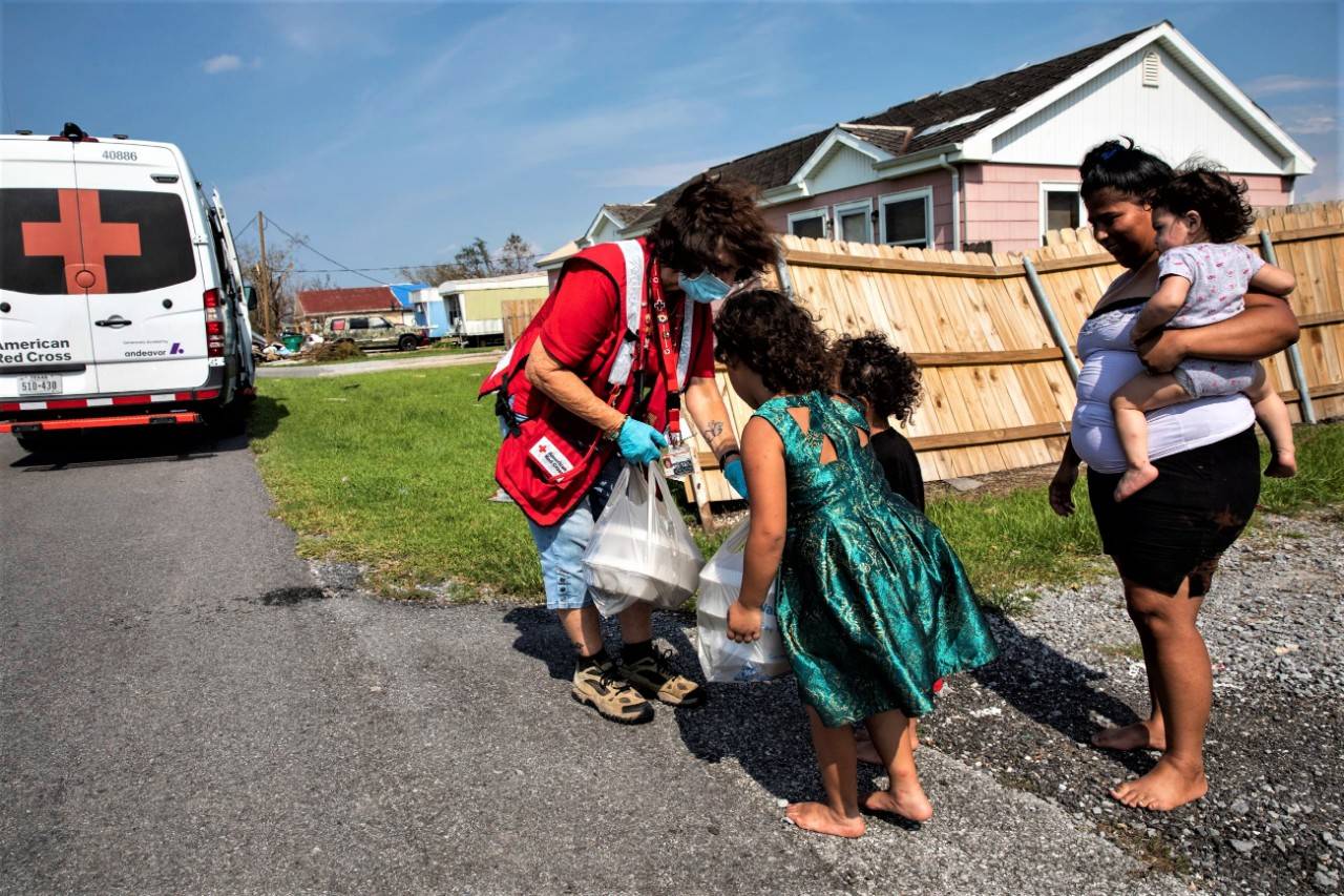 September 3, 2021. Larose, Louisiana. American Red Cross volunteer Marjie Day delivers warm meals to Yvonne Padilla Lucca and her four children whose home was damaged and left without power by Hurricane Ida, in Larose, Louisiana on September 3, 2021. The Red Cross is working with partners to prepare tens of thousands of meals that are being delivered by our Emergency Response Vehicles to the people in the hardest hit areas struggling to recover. With the help of partners, as of September 3, 2021, the Red Cross has already provided some 49,500 meals and snacks and distributed more than 16,000 relief items. Photo by Scott Dalton/American Red Cross