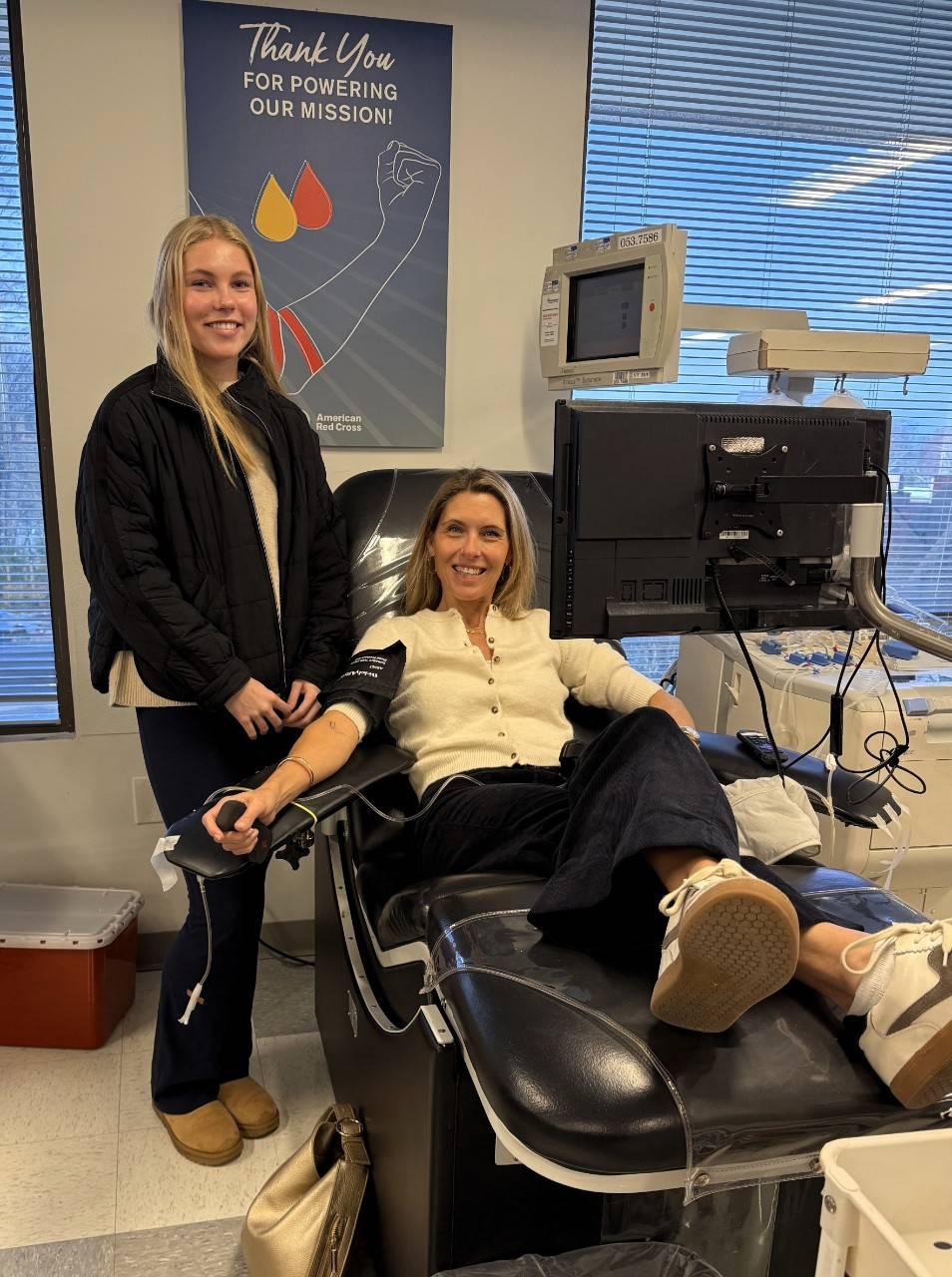 Lisa Malloy seated in a Red Cross blood donation chair with her daughter standing next to her