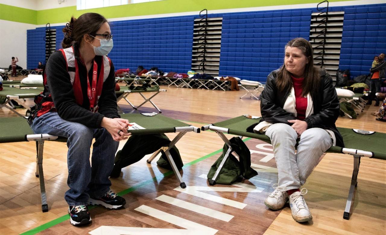 December 12, 2021. Bowling Green, Kentucky.
Sharon Wilson speaks to Red Cross volunteer Amy Miller and explains what happened to her last Saturday morning. Sharon heard the tornado sirens early Saturday morning in Bowling Green, Kentucky. She looked outside her window but didn’t see a lot happening so she continued what she was doing. A little later she looked out her window again and she could see a tornado warning beacon flashing in the distance. This time she headed the warning and ran for cover in her bathtub and hoped for the best. Not long after she could hear a roar of wind and debris falling while the whole house shook. Right after the tornado passed a neighbor came to the house. “Are you alright?” he called out to her. “I don’t know” she replied, “I’m here in the bathroom”. “When I got out, I saw how it had ruined my home. The walls of my bedroom had collapsed, the roof was damaged and rain was pouring in. My front door was gone and my living room was now an outdoor space,” she says. Although her home of 17 years was now a shambles, Sharon was left uninjured. “The only thing I can do now is rebuild,” she says. But for the time being, home is now at the American Red Cross managed shelter at Jennings Creek Elementary School in Bowling Green, Kentucky.
Photo by Marko Kokic/American Red Cross