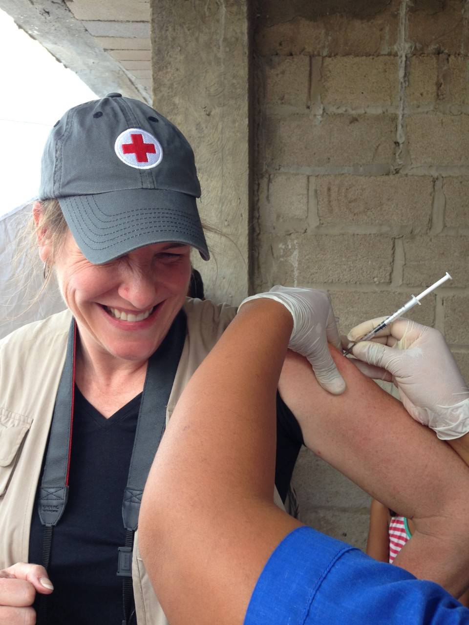 A woman in a Red Cross hat grimaces as a health worker gives her a flu vaccination in her arm.