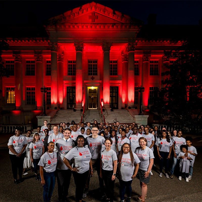 Group of Red Cross volunteers in front of red lit American Red Cross headquarters