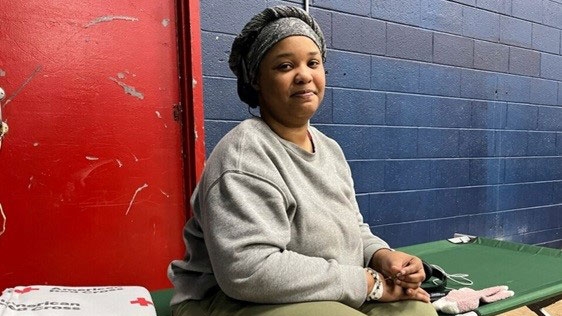 Chelsea Constance sitting on a cot with a Red Cross blanket in a shelter.