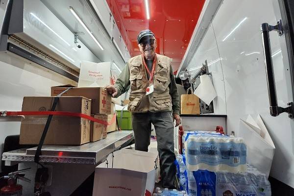 Red Cross volunteer in the back of an EVR filled with water bottles and boxes.