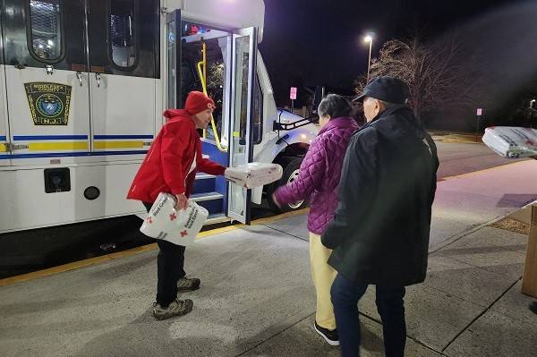 Red Cross volunteer handing out wrapped blankets to people on street.