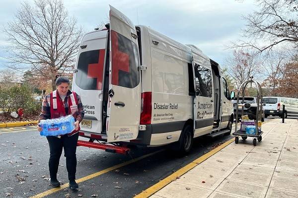 Red Cross volunteer carrying case of bottled water from Red Cross vehicle.
