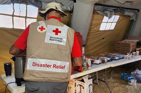 Red Cross volunteer getting coffee at a table full of drinks and snacks.