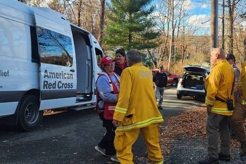 Red Cross volunteers and firefighters on the side of the road next to a forest.