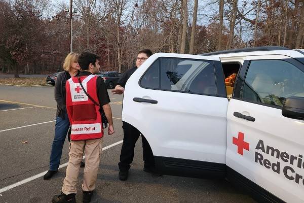 Red Cross volunteers next to a Red Cross vehicle in a parking lot next to a forest.