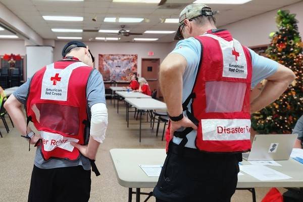 Two red cross volunteers looking at paperwork that's on a folding table.