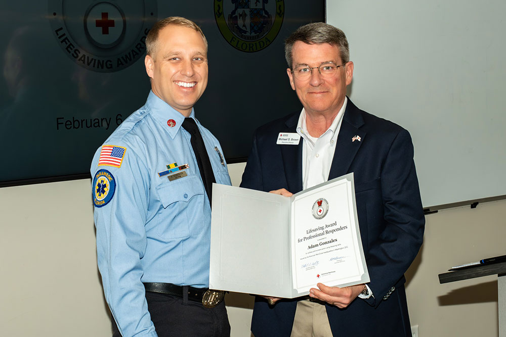 AJ Gonzales holding a lifesaving award while standing next to Mike Brown, executive director of the Tampa Bay area for the American Red Cross.