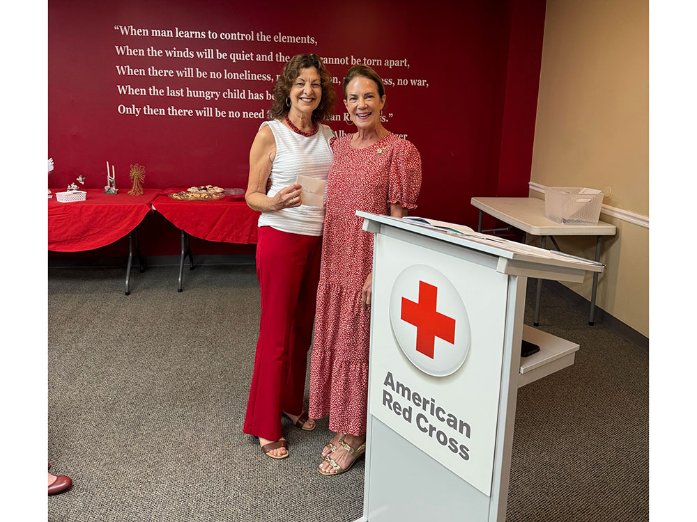 two Red Cross staff members, one holding a napkin with a name written on it, and smiling for picture.