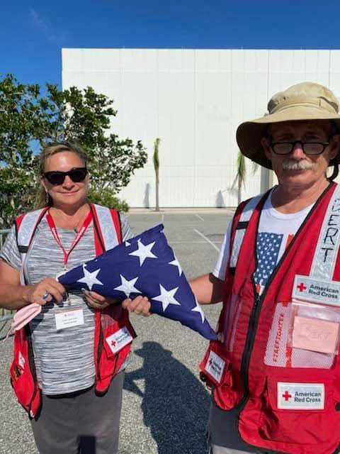 two Red Cross volunteers outside standing in a parking lot holding a folded American flag.