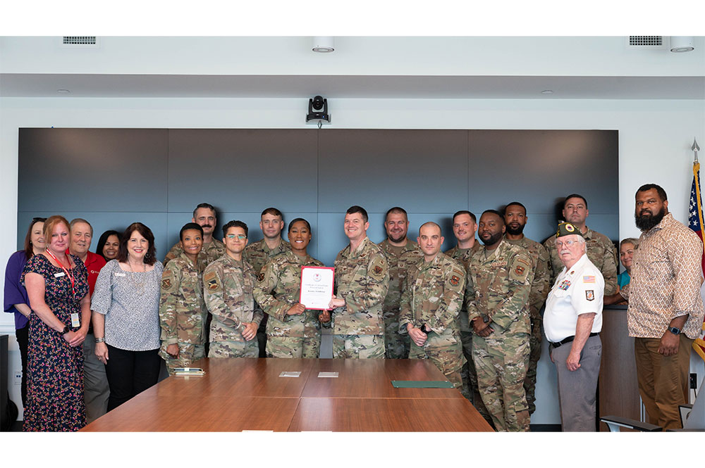 Keosha Middleton, wearing military clothes, displays her Red Cross award with group military members and Red Cross staff members in a conference room.