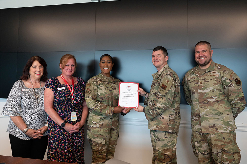 Keosha Middleton, wearing military clothes, displays her Red Cross award with two other military members and two Red Cross staff members in a conference room.