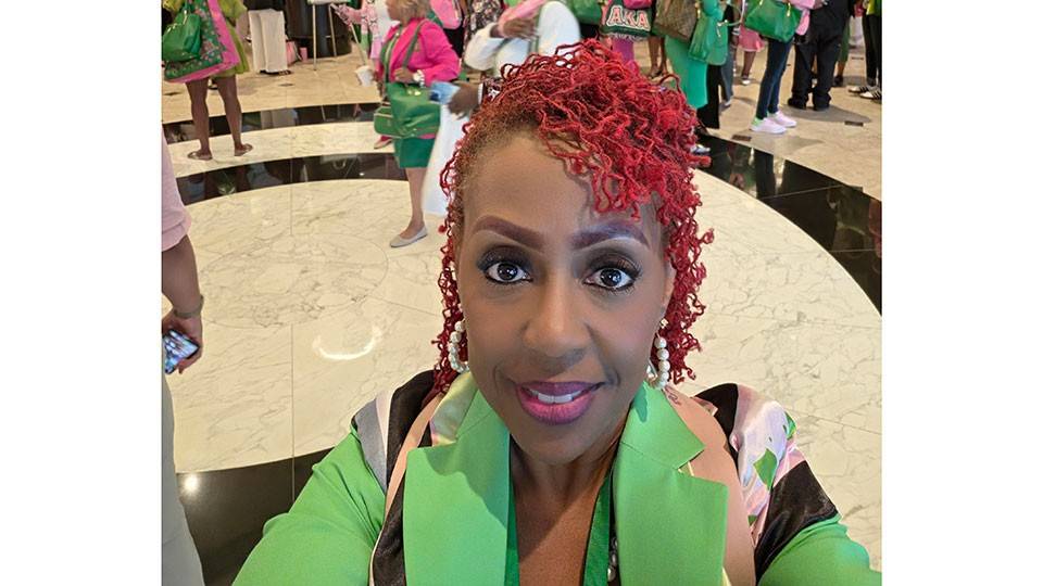 Dr. Andrea Pullen selfie wearing a green blazer with lots of people in the background in a room with marble floors.