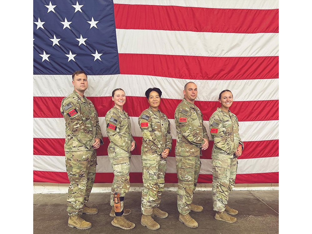 Angelica Sowynn and four others in military camo with a large American flag behind them.