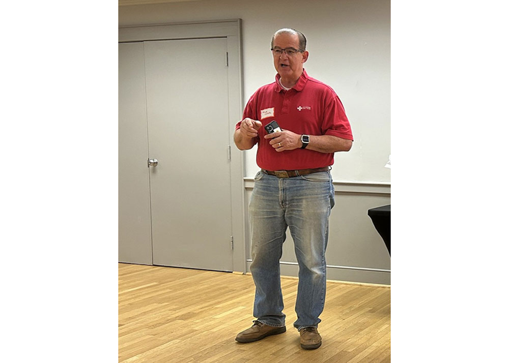 Frank Castillo wearing glasses and a Red Cross shirt speaking in a room.