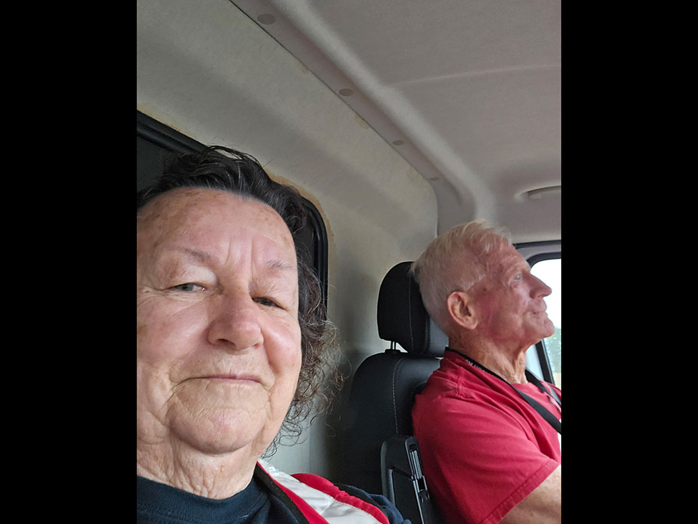 Red Cross volunteer Helen Miller takes a selfie in her emergency response vehicle with another volunteer in the driver's seat.