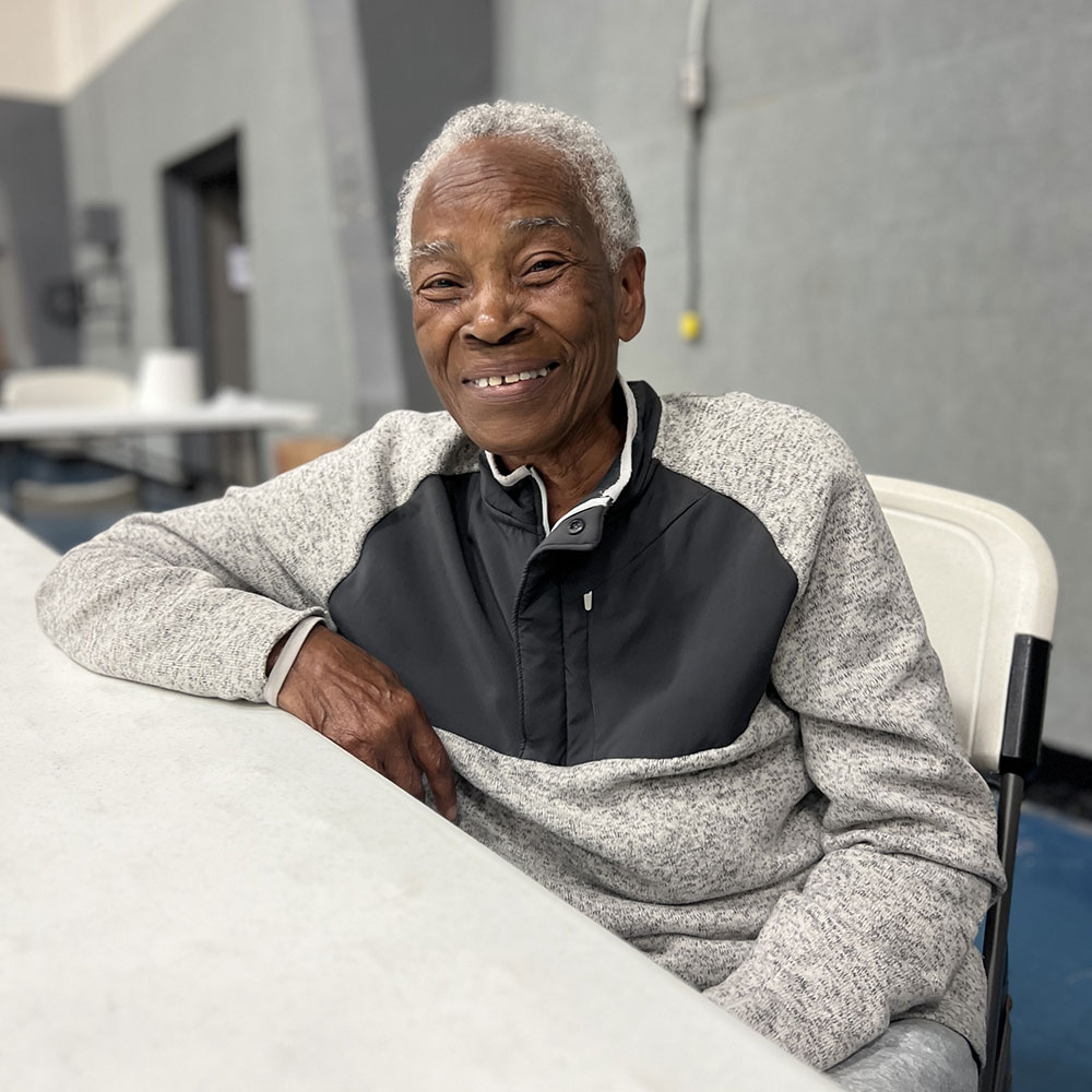 Maggie Harris sitting in a chair next to a table and smiling for picture.