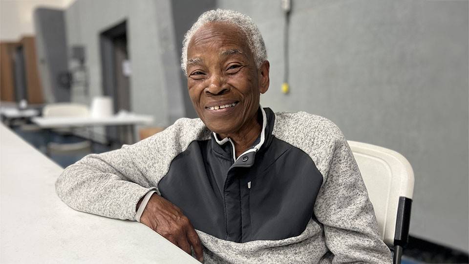 Maggie Harris sitting in a chair next to a table and smiling for picture.