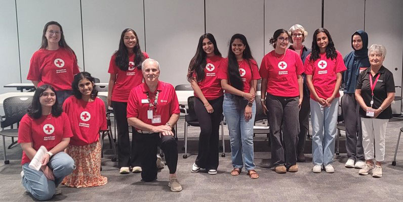 A group of Red Cross volunteers, are standing and kneeling in a room, smiling.