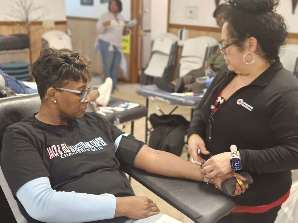 A woman donates blood in a community center. A Red Cross nurse prepares her arm for donation.