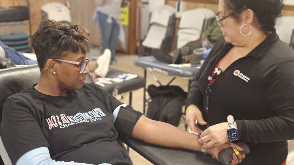 A woman donates blood in a community center. A Red Cross nurse prepares her arm for donation.