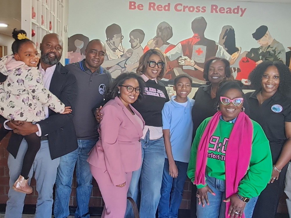 A diverse group of people smiling and posing in front of a "Be Red Cross Ready" mural.