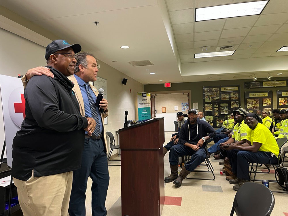 Reginald LaMon and ARC NC Exec. Dir. Jason Gudzunas stand at a podium in a room, one with a microphone. Seated people in safety uniforms listen.