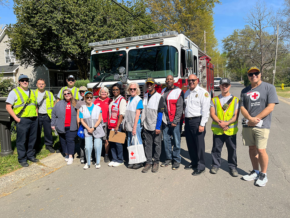 group photo of CMAC Exec. Dir. Jason Gudzunas with Charlotte Fire Chief Reggie Johnson, community partners and volunteers standing in front of a fire engine.