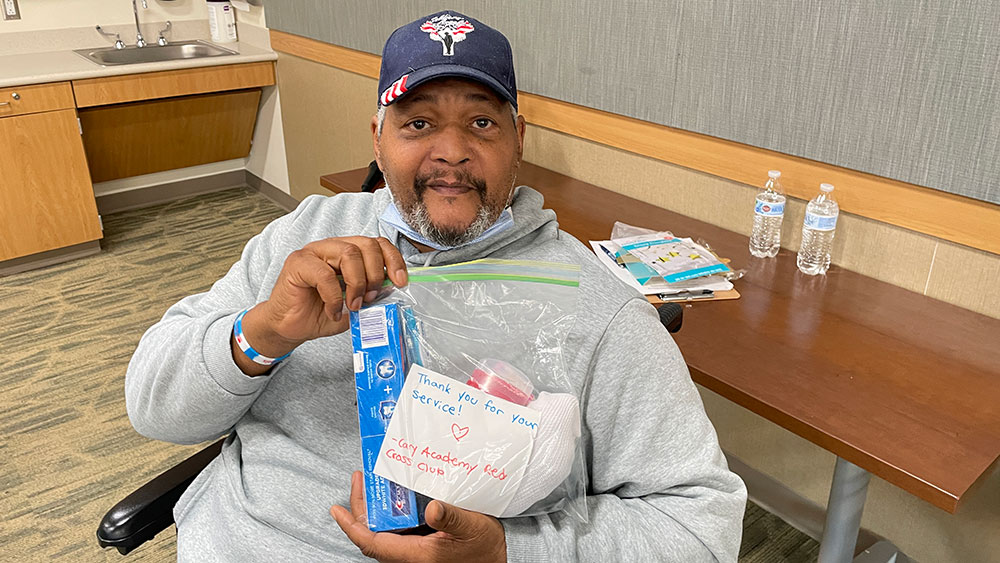 Veteran in wheelchair showing items received from Red Cross HS Club event.