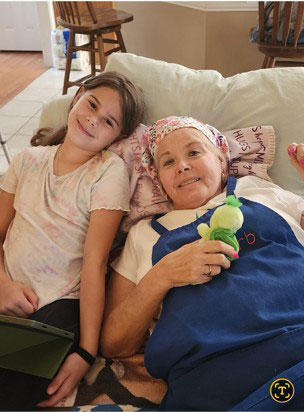 A young girl and Sherry Kemp lie on a couch. Sherry smiles while holding a small green toy.