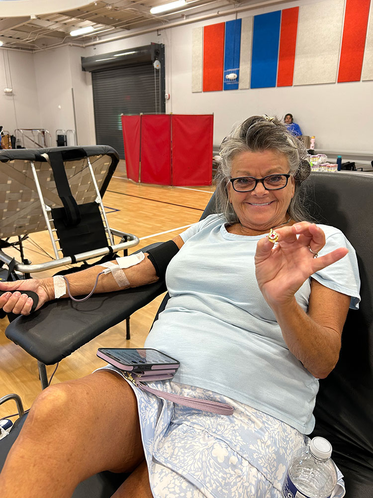 Sandra Ammons donating blood and holding a red cross pin.