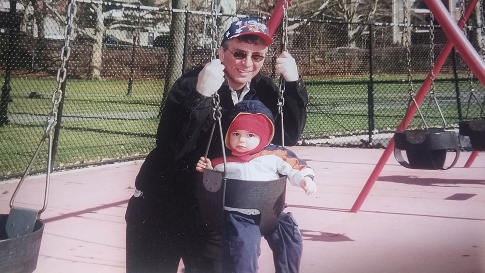Stephen Agnelli standing next to his son Daniel in a swing on a playground.