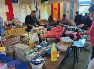 room of tables with packaged food, cleaning supplies, and other items with people looking through them.